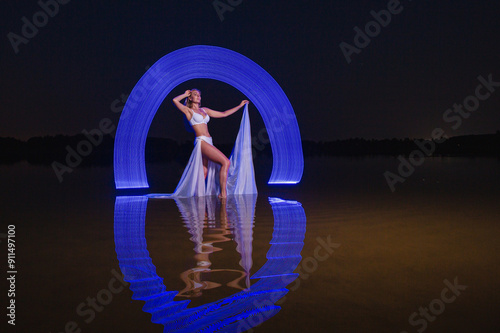 Obraz na płótnie Young slim girl in white swimsuit posing in water at night with abstract blue light effect w salonie