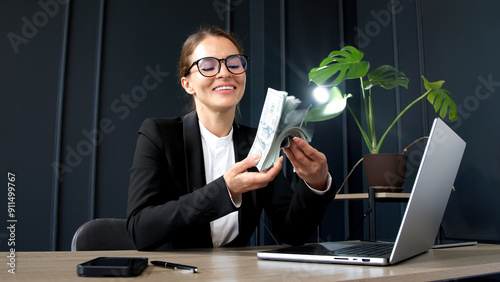 A confident and successful businesswoman celebrates a lucrative deal with a stack of money in her modern office. Perfect for themes of business success, financial achievement, and professionalism.
