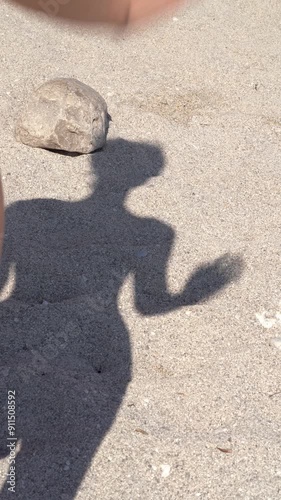 Shadow of a young woman waving her hand on the sand with stones on the beach in the middle of the day. Concept of summer memories and authentic pastime, UGC