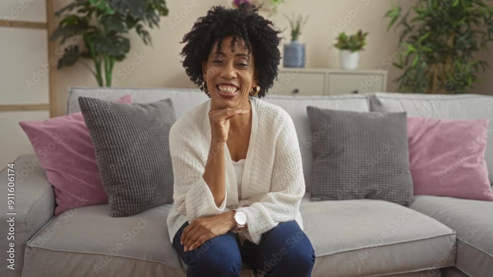 A beautiful young african american woman with curly hair sitting in a cozy living room, smiling and wearing casual white attire, surrounded by soft pillows and indoor plants. A beautiful young african american woman with curly hair sitting in a cozy living room, smiling and wearing casual white attire, surrounded by soft pillows and indoor plants.