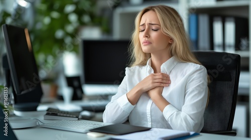 A stressed young businesswoman holding her chest, sitting at a desk with a worried expression, indicating health anxiety or work pressure. photo