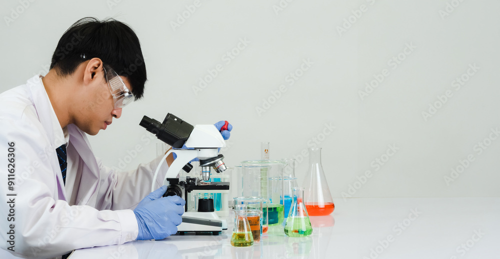 Fototapeta premium Portrait asian man student scientist Wearing a doctor gown in the lab looking hand at chemist. caused by mixing reagents in scientific research laboratories with test tubes and microscope on the table