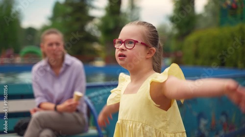 Young girl with Down syndrome, holding ice cream, blows kiss to her mother off-camera and smiles. Scene captures loving and joyful moments of raising child with special needs photo