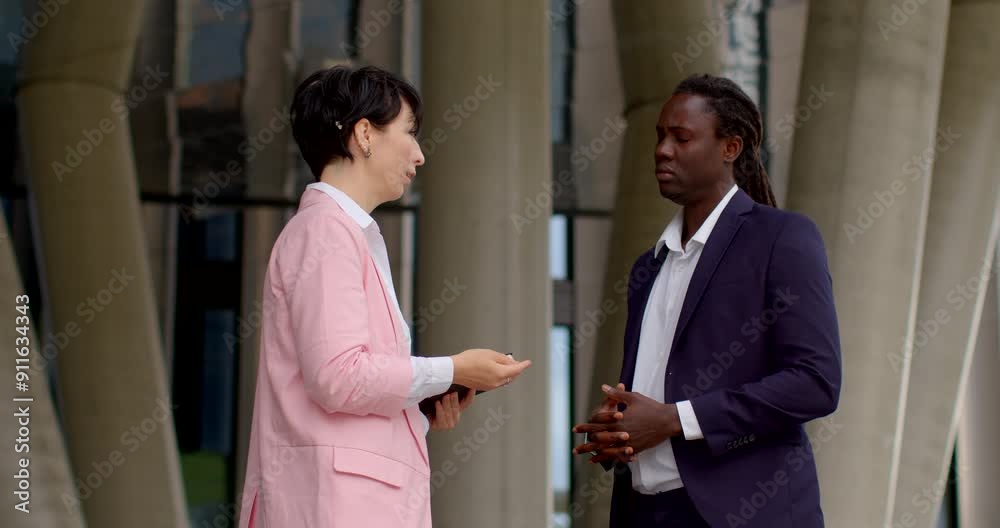 Two professionals engage in a business conversation outdoors, showcasing collaboration and professionalism He listens to the woman in the pink jacket. Getting an opinion.