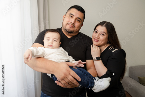 Small family spending time at home - happy dad mom and baby - dad holding his son while his wife hugs him - hispanic family