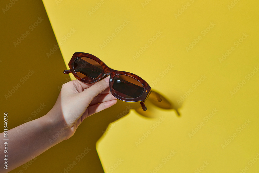 Female hands holding stylish sunglasses on yellow background Female hands holding stylish sunglasses on yellow background