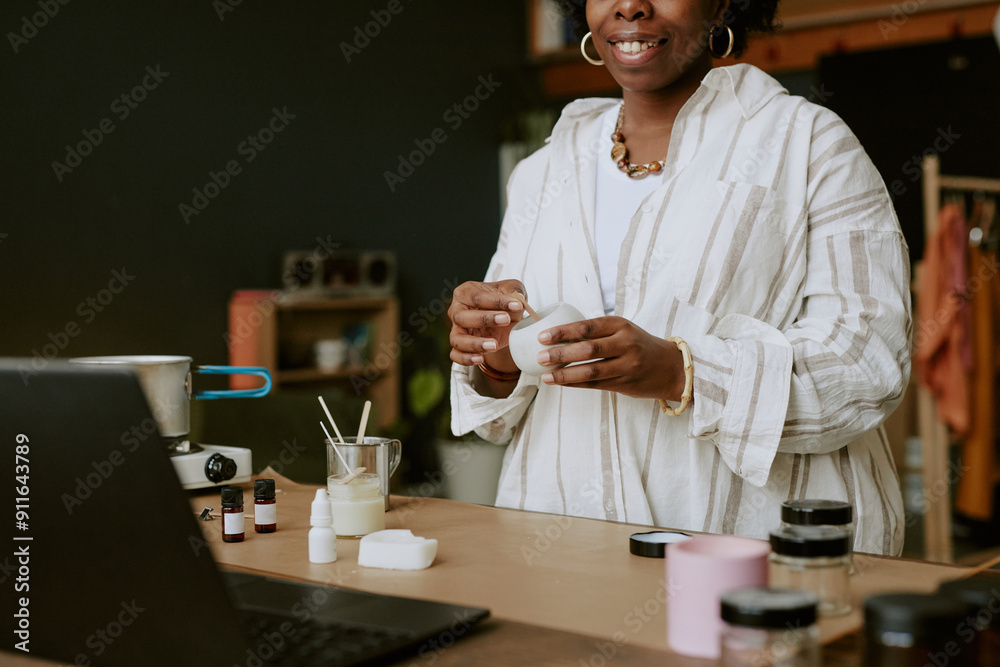 Smiling woman holding mug while standing in cozy workspace with various items on desk creating a warm and inviting atmosphere Smiling woman holding mug while standing in cozy workspace with various items on desk creating a warm and inviting atmosphere