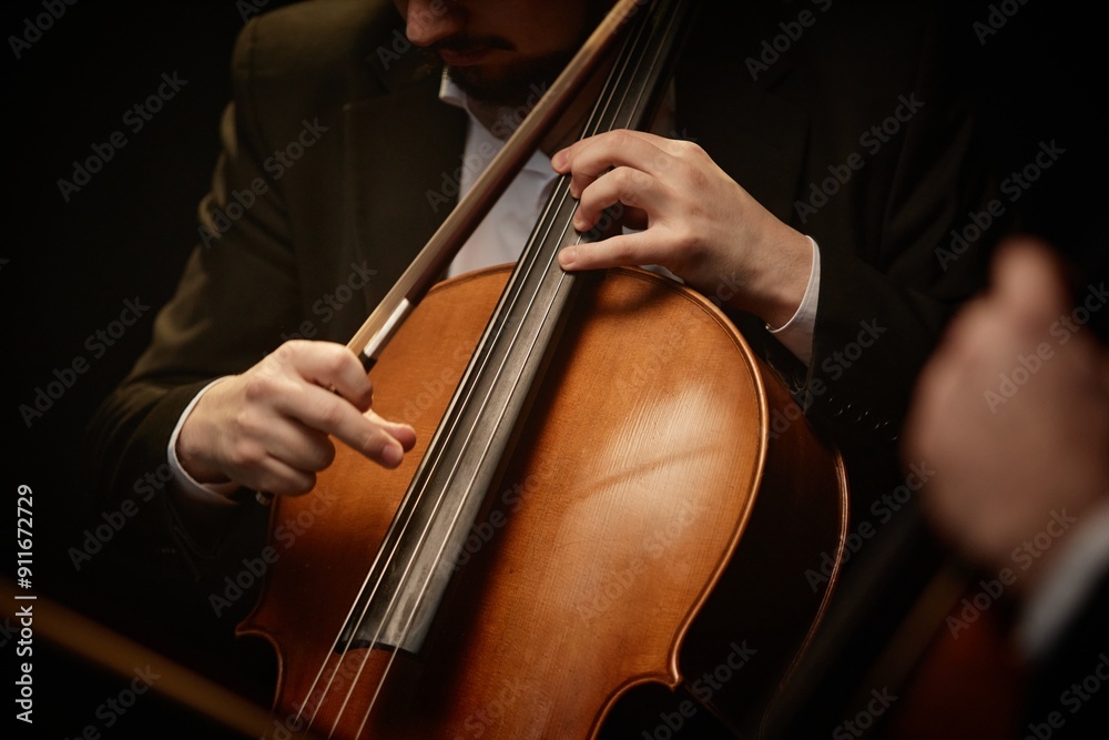 Close up on hand of unrecognizable devoted male musician strumming cello while playing with chamber quartet in dramatic light, focus on fingers and strings Close up on hand of unrecognizable devoted male musician strumming cello while playing with chamber quartet in dramatic light, focus on fingers and strings