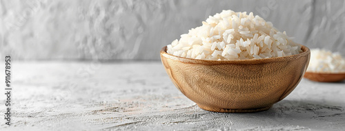 wide side view background cover image of boiled white rice in a natural color wooden bowl in white table with raw rice around 