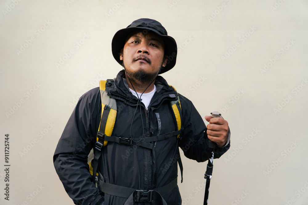 Photo of Asian man wearing adventurer outfit. Half body portrait of an adventurer doing many poses while wearing jacket, hat, backpack and trekking poles isolated on beige background Photo of Asian man wearing adventurer outfit. Half body portrait of an adventurer doing many poses while wearing jacket, hat, backpack and trekking poles isolated on beige background 