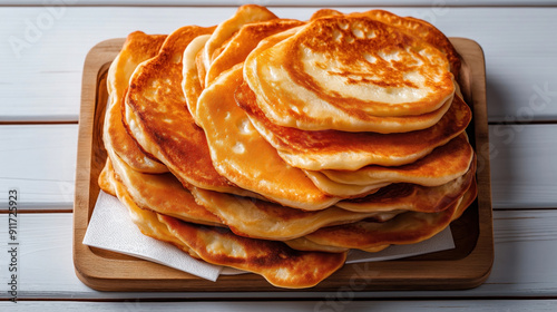 Traditional Russian food Oladi. These are small, thick pancakes with a golden-brown exterior, layered on a wooden board with a paper napkin underneath.