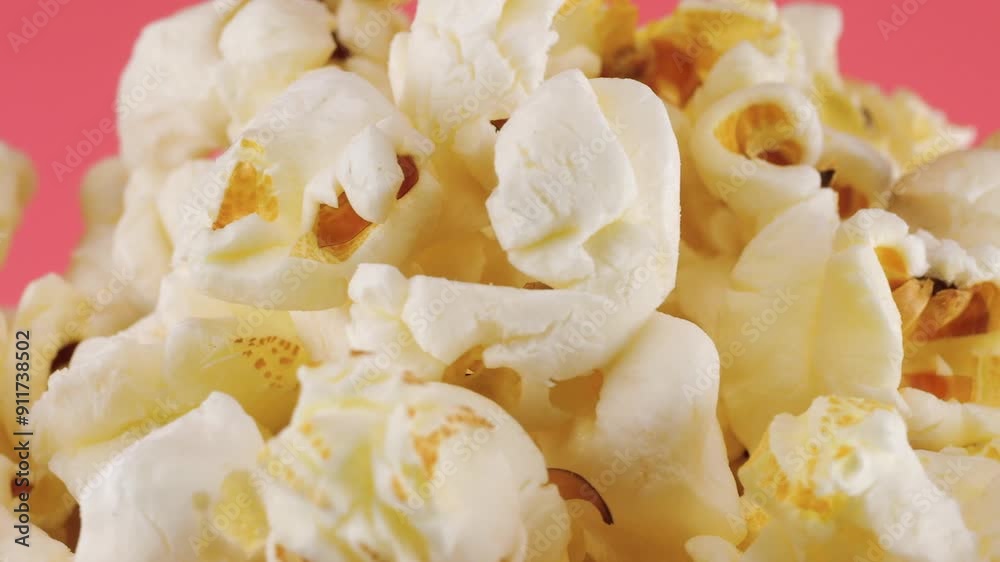 Popcorn grains rotating in a red and white striped bucket isolated on pink background. Movie snack food, fast food cafe sweet snack. Popcorn grains rotating in a red and white striped bucket isolated on pink background. Movie snack food, fast food cafe sweet snack.