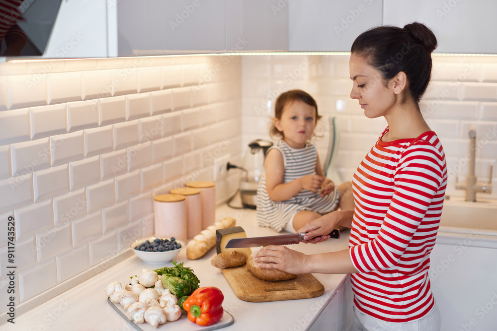 mother and cute little child daughter preparing breakfast in modern white kitchen. mom cutting bread on table. mother and cute little child daughter preparing breakfast in modern white kitchen. mom cutting bread on table.