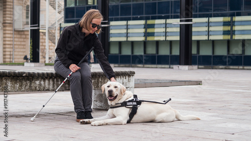Foto Blind or visually impaired woman resting with her guide dog on the bench on a city street