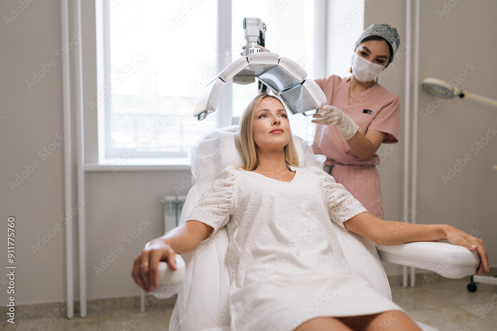 Wide shot of beautician specialist in mask connecting and adjusting innovation device for photodynamic therapy procedure during hair treatment at modern medical clinic. Concept of esthetic care. Wide shot of beautician specialist in mask connecting and adjusting innovation device for photodynamic therapy procedure during hair treatment at modern medical clinic. Concept of esthetic care.