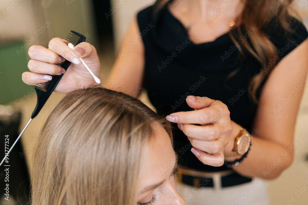 Fototapeta premium Cropped shot of unrecognizable hairdresser applying peeling purifying and soothing cosmetics product to scalp using cotton swabs. Blonde female client having beauty salon service treatment.