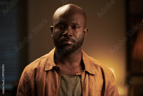 Young bald serious African American man with beard looking at camera while standing in home environment during argument photo