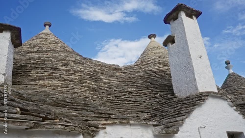 Traditional trullo house in alberobello, italy, showing characteristic stone roof and white chimney under a blue sky photo