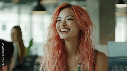髪の毛がピンク色の女性がオフィスで友人と楽しそうに会話しながら笑っている様子。