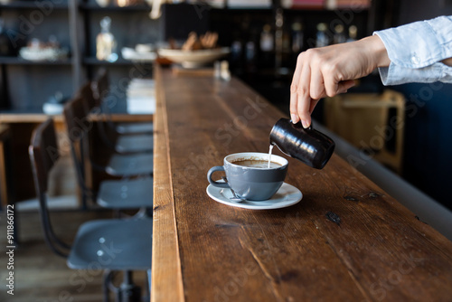 Waiter Pouring Milk To Coffee Cup In Restaurant photo