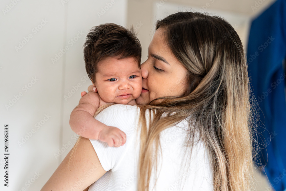 Young mother kissing crying newborn baby on shoulder Young mother kissing crying newborn baby on shoulder