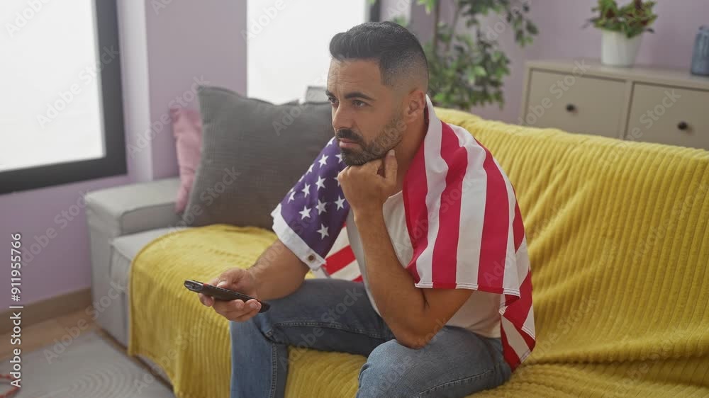 Pensive hispanic man with american flag draped over shoulders watching tv in his apartment living room Pensive hispanic man with american flag draped over shoulders watching tv in his apartment living room