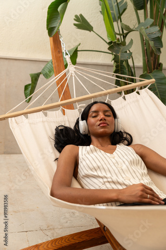 Woman relaxing in a hammock with headphones in tropical indoor setting photo