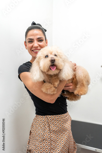 Professional pet groomer holding adorable poodle in grooming salon