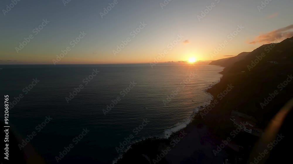 Scenic sunset on horizon over water. Drone view descending to just above surface and rocks in sea. Hillside homes and cliffs of Madeira shoreline. Scenic sunset on horizon over water. Drone view descending to just above surface and rocks in sea. Hillside homes and cliffs of Madeira shoreline.