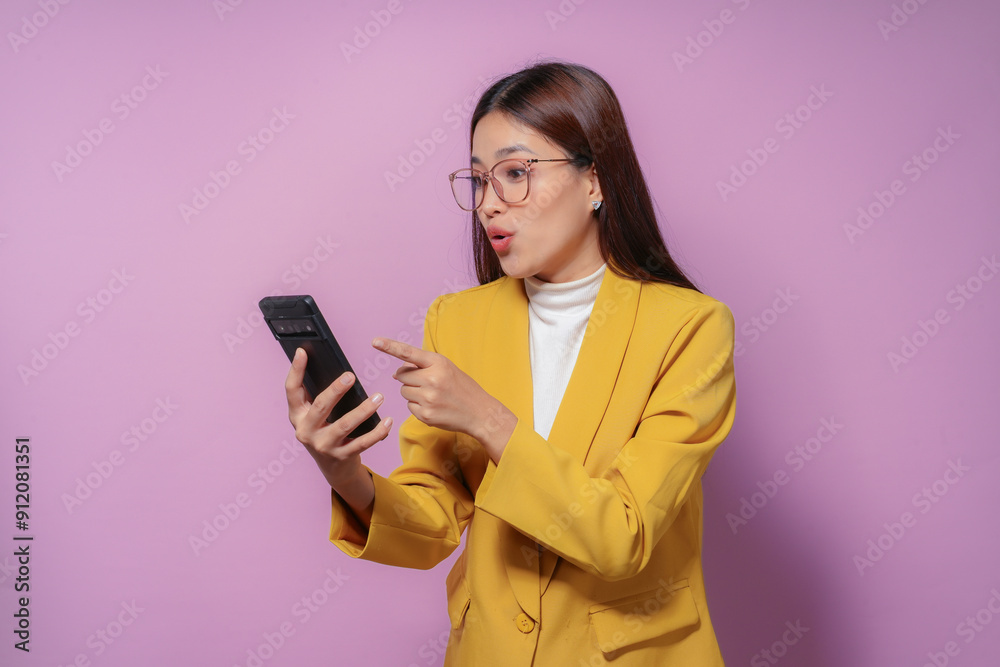 Surprised businesswoman wearing a yellow blazer pointing at her smartphone with a shocked expression on a purple background Surprised businesswoman wearing a yellow blazer pointing at her smartphone with a shocked expression on a purple background
