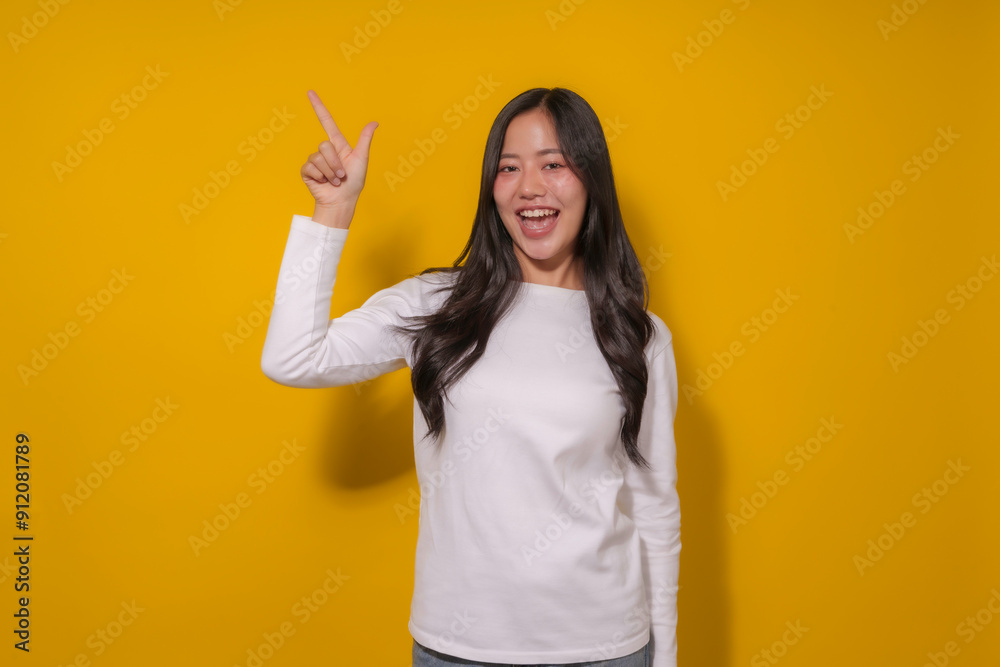 Young woman with long dark hair is smiling and pointing to her left against a vibrant yellow background Young woman with long dark hair is smiling and pointing to her left against a vibrant yellow background