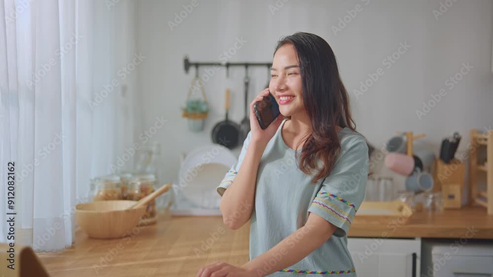 Asian attractive woman talking on mobile phone device in kitchen at home. Asian attractive woman talking on mobile phone device in kitchen at home.