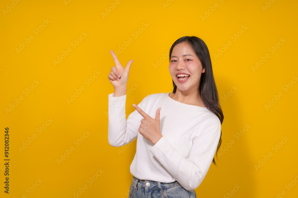 Young woman is smiling and pointing with both hands to the side on a yellow background Young woman is smiling and pointing with both hands to the side on a yellow background