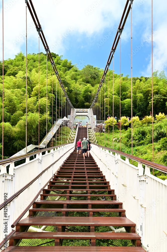 Obraz premium Taiwan - Jul 07, 2024: Visitors ascend and stroll on the Taiping Suspension Bridge under clear skies, surrounded by lush greenery and expansive natural beauty.