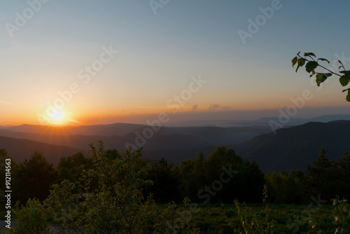 Golden sunset over hills and forests with clear sky.