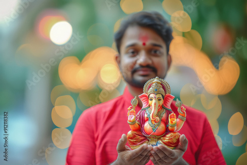 Young indian man in traditional wear holding lord ganesha sculpture in hand photo