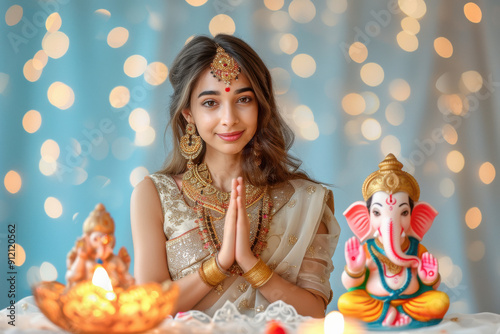 young Indian woman wearing cream colour dress and prayer, and side table a big colourful and beautiful lord Ganesha statue. photo