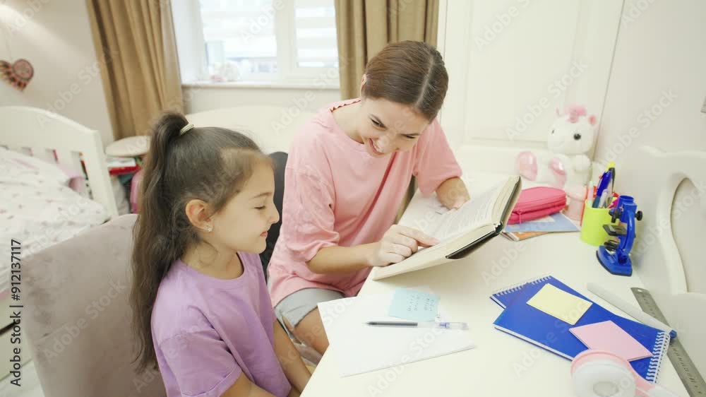 A caring mother helps her daughter with her homework in a warm, cozy children's room at a desk filled with colorful stationery and teaching aids. A caring mother helps her daughter with her homework in a warm, cozy children's room at a desk filled with colorful stationery and teaching aids.