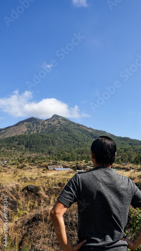 Back view of a male tourist or traveler looking at Mount Batur in Bali, Indonesia. Beautiful view under a clear sky, perfect for travel and nature themes, highlighting adventure and exploration