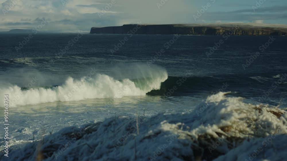 and ice covers coastal grass as ocean waves catch early morning light below cliffs as surfers chase waves, slow motion and ice covers coastal grass as ocean waves catch early morning light below cliffs as surfers chase waves, slow motion