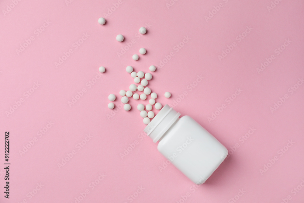 Homeopathic remedy. Overturned plastic bottle and pills on pink background, top view Homeopathic remedy. Overturned plastic bottle and pills on pink background, top view