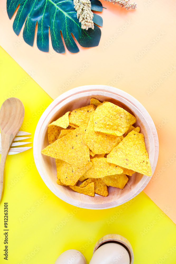 Corn chips on wooden plate isolated on orange and yellow background. Crispy snack dessert. Food Photography Concept