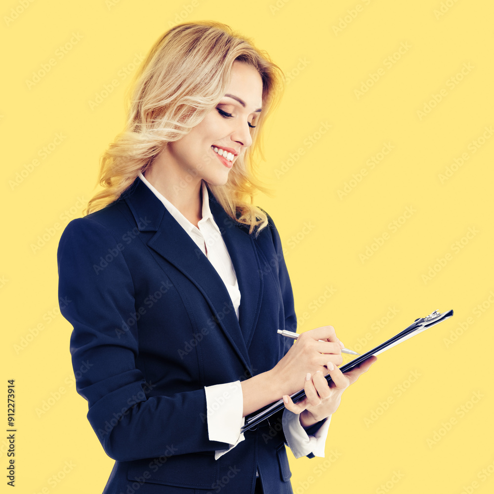 Young beautiful businesswoman wear confident suit, with clipboard writing, isolated on yellow color background. Business studio concept image. Square. Young beautiful businesswoman wear confident suit, with clipboard writing, isolated on yellow color background. Business studio concept image. Square.