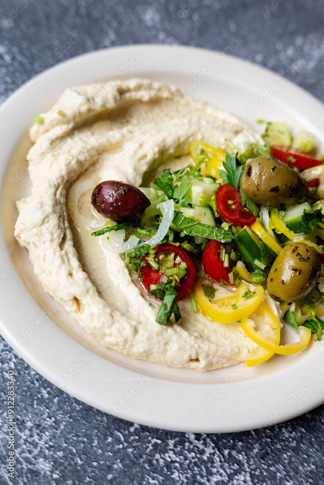 traditional hummus loaded with fresh cucumbers, olives, tomatoes, pepper, onions and herbs on plate on dark grey table, flat lay, close-up traditional hummus loaded with fresh cucumbers, olives, tomatoes, pepper, onions and herbs on plate on dark grey table, flat lay, close-up
