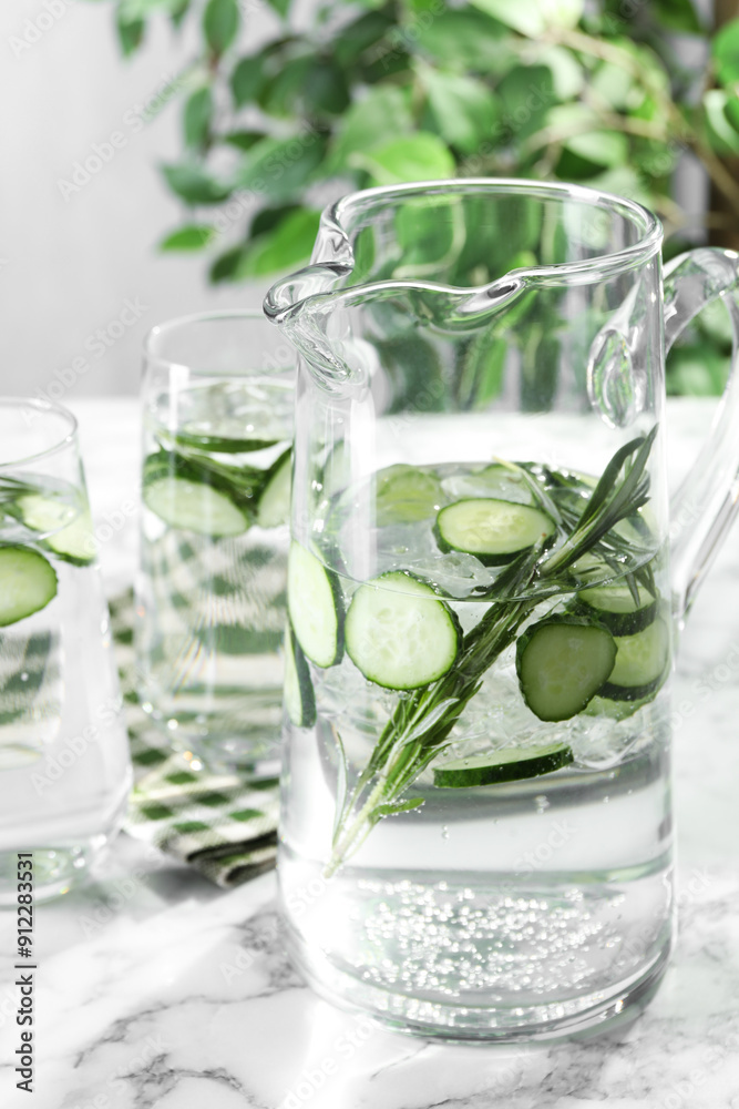 Refreshing cucumber water with rosemary in jug and glasses on white marble table, closeup Refreshing cucumber water with rosemary in jug and glasses on white marble table, closeup