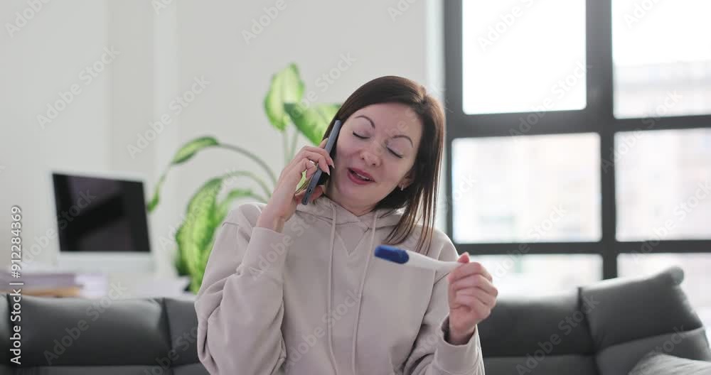 Smiling woman at home talking on phone and looking at pregnancy test Smiling woman at home talking on phone and looking at pregnancy test