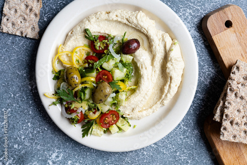 Traditional hummus served with olives, cucumbers, tomatoes, pepper and herbs on dark bachground, close up photo