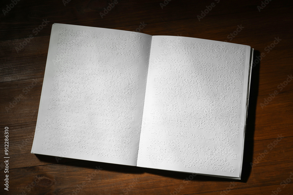 Fototapeta premium Book with Braille text on wooden table, top view. Education and leisure for blind people