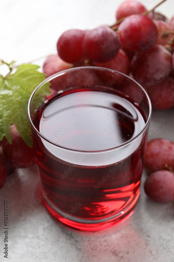 Tasty grape juice in glass, leaf and berries on light textured table, closeup Tasty grape juice in glass, leaf and berries on light textured table, closeup