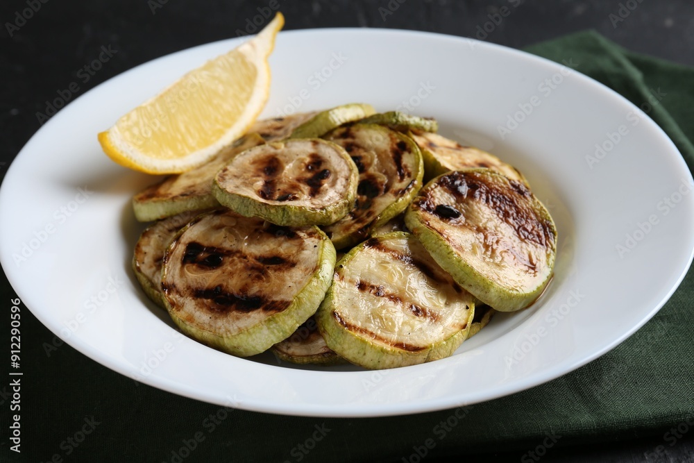 Tasty grilled zucchini slices with lemon on black table Tasty grilled zucchini slices with lemon on black table